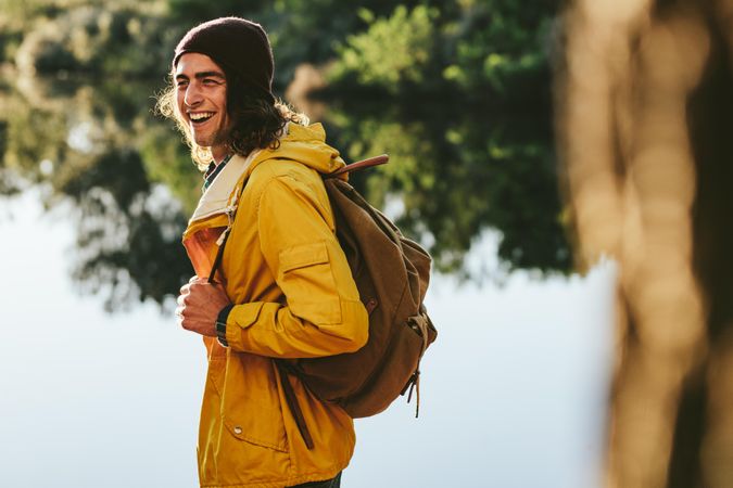Man wearing backpack and jacket laughing while walking outdoors