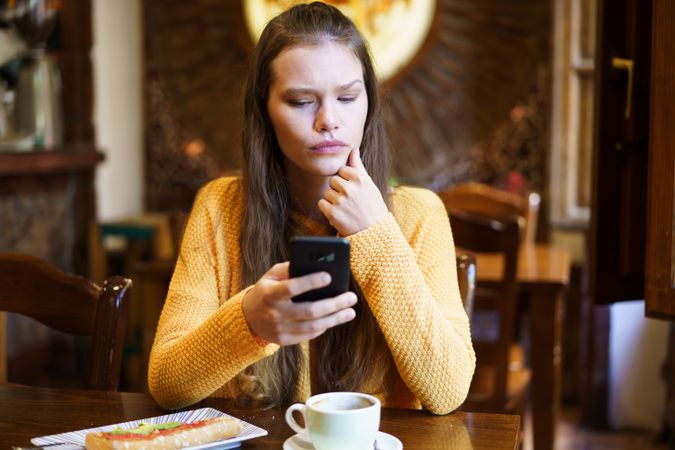 Young Woman Engaged with Smartphone in Cozy Cafe Setting