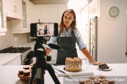 Female pastry chef vlogging with mobile phone mounted on tripod in kitchen 499kE4