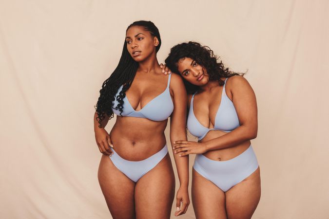 Two young women standing together embracing their natural bodies and curves in studio