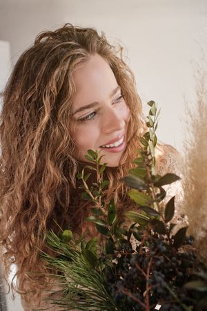 Positive blond lady near green plants in studio