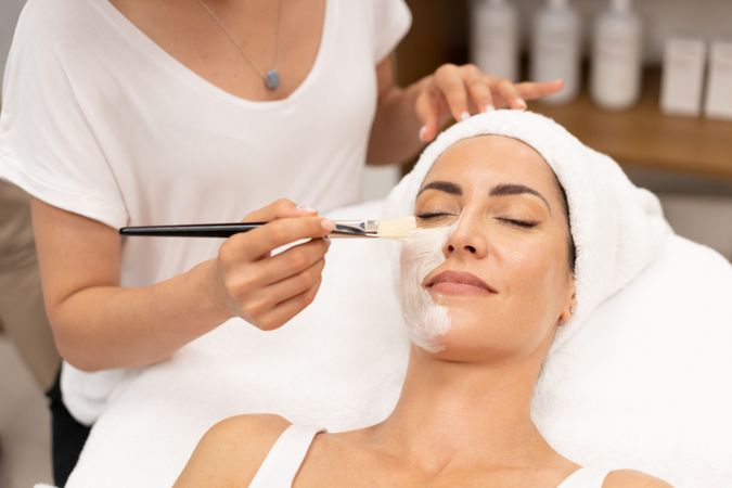 Woman with towel on head having a relaxing face mask applied at salon