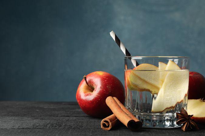 Sideview of glass of water with straw, apple slices and cinnamon slices with copy space