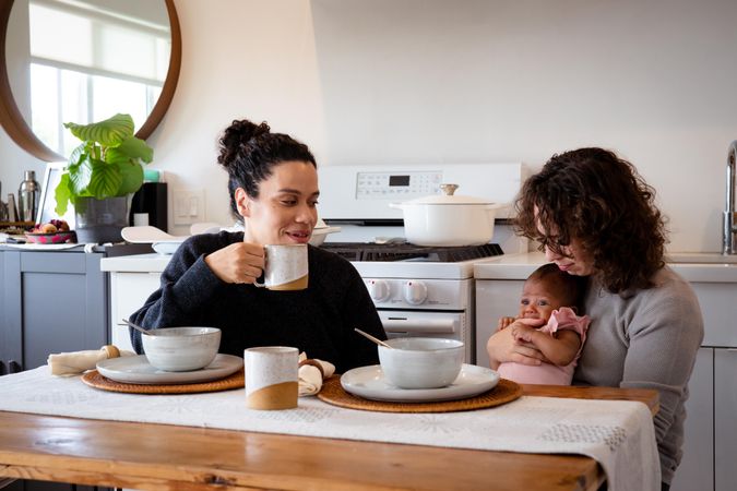Two women eating soup and drinking coffee with newborn baby at their dining table