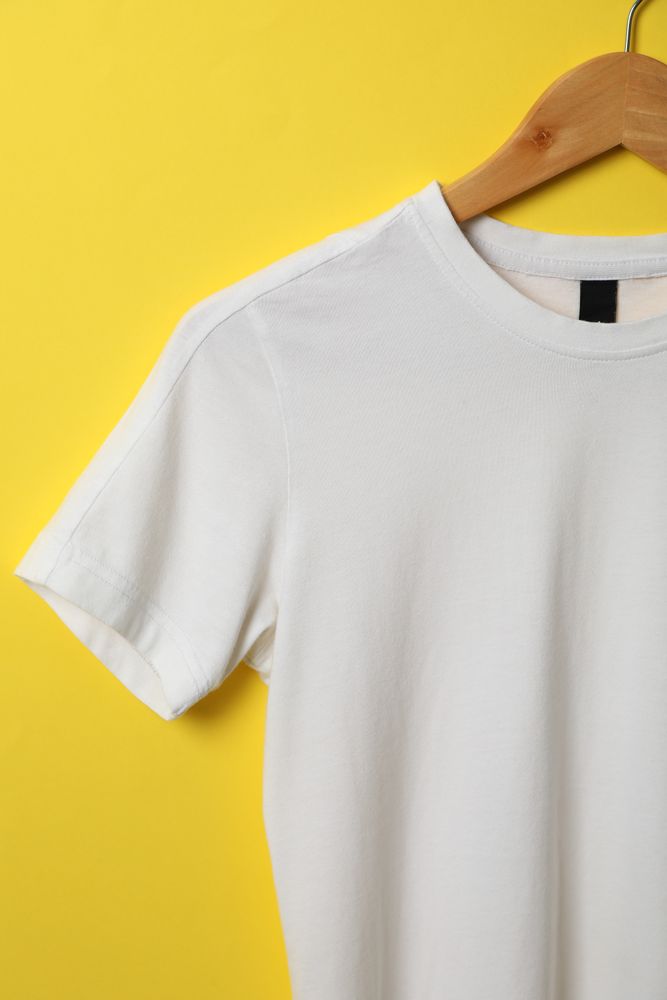 Hanger with blank t-shirt on yellow background, space for text