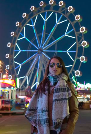 Smiling young woman near illuminated ferris wheel at night