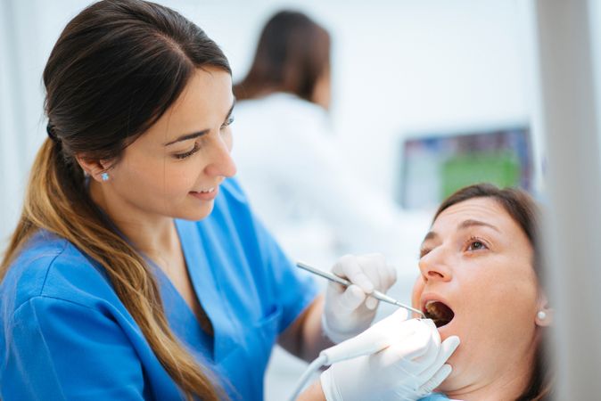 Dentist and assistant examining mouth of patient in chair with tools