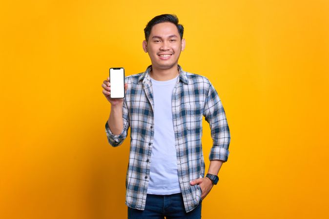 Asian male smiling with hand in pocket and showing blank screen of smart phone