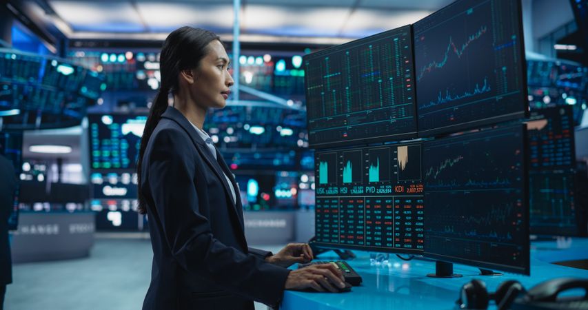 Young Female Stock Exchange Broker Working on Computer with Multi-Screen Workstation with Real-Time Stocks, Commodities and Exchange Market Charts.