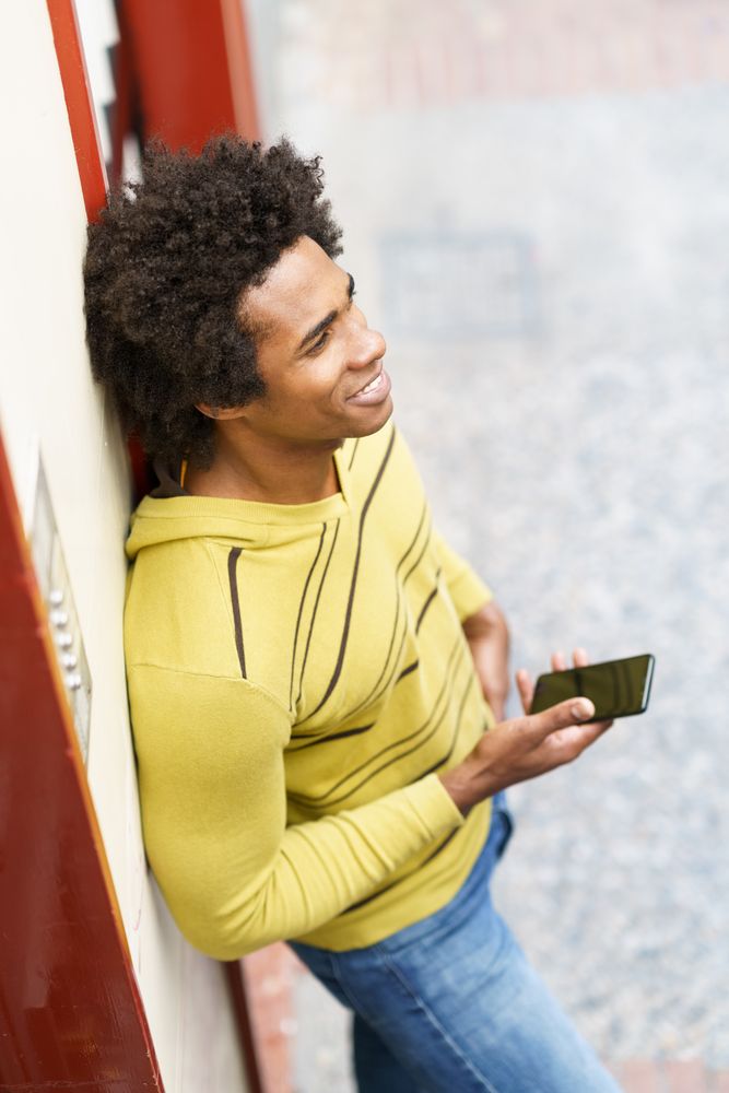 Smiling man leaning on wall outside with phone in hand