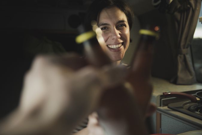 Smiling woman clanging bottles with person near cooker in camper van