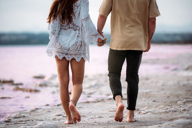 back view of adorable couple walking on an amazing beach with pink water