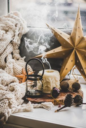 Extinguished candle, festive gold star and pine cone decorations with woolen blanket