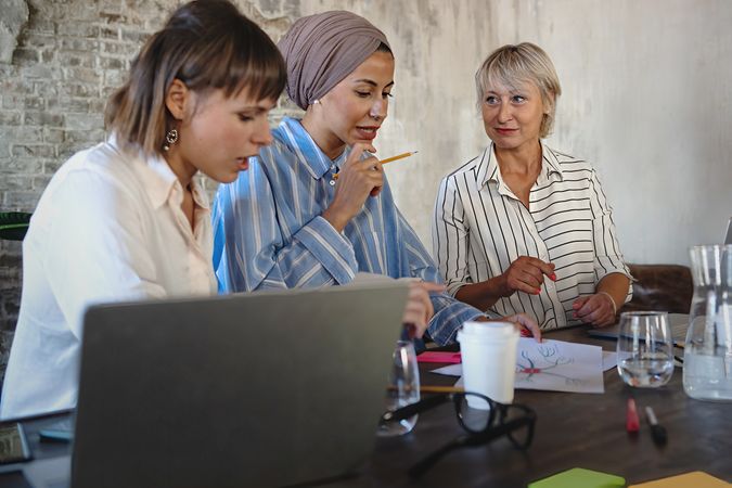 Three women collaborate in an office, one wearing a headwrap