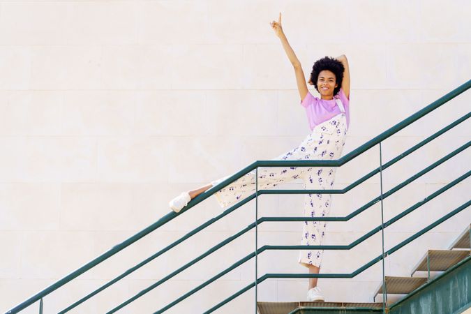 Happy woman on stairs with leg up on green handrail and arm up