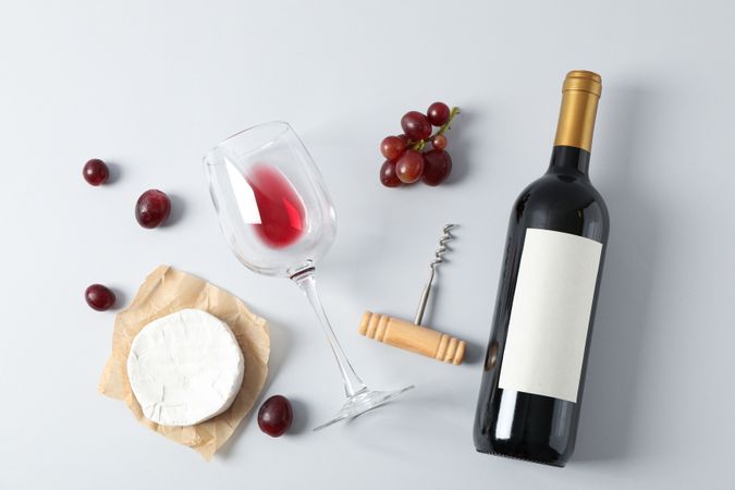 Flat lay. Grapes, cheese, corkscrew, bottle and glass with wine on grey background, copy space