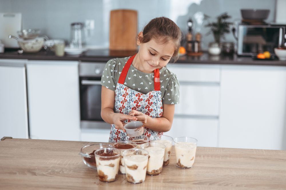 tiramisu making process in the kitchen- little girl making Italian desert with cocoa and espresso-dipped ladyfingers with mascarpone cream