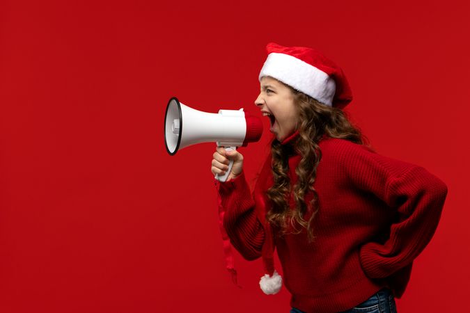 Energetic girl in Santa hat and sweater shouts into megaphone