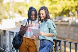 Women friends using tablet in casual clothing outside