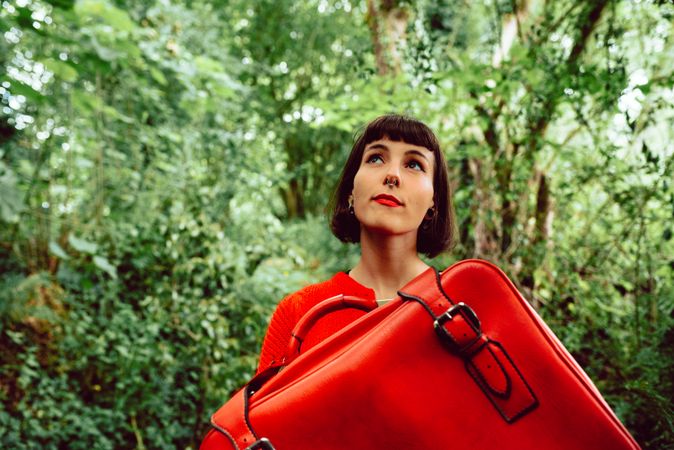 Woman in red with big red suitcase in forest