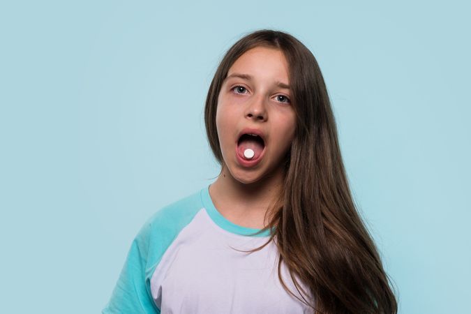 Girl holds pill on tongue, preparing to take medication.
