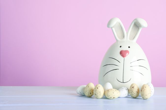 Decorated bunny and Easter eggs on table against color background. Space for text
