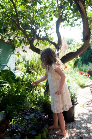 Young girl reaching for a plant in yard