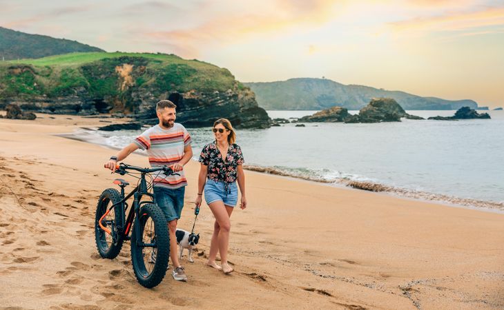Man and woman walking along the coast with bicycle and small dog