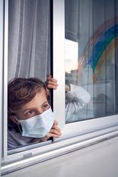 Boy in medical mask looking out window