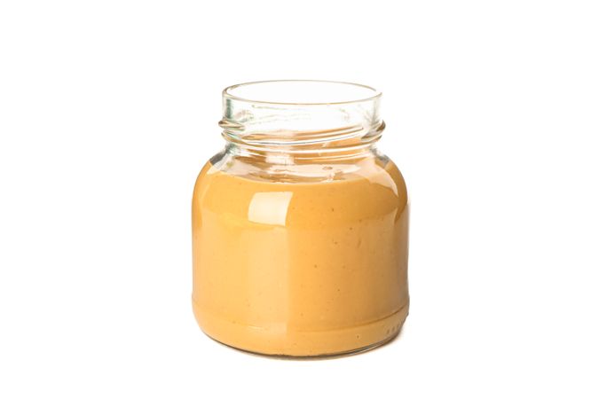 Creamy peanut butter in glass jar isolated on light background. A traditional product of American cuisine