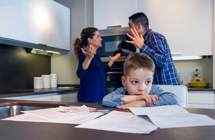 Couple fighting in front of son with bills strewn on the kitchen counter