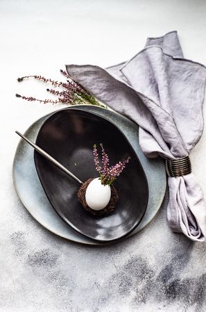 Top view of elegant Easter table with heather and egg decor on dark plate on grey counter