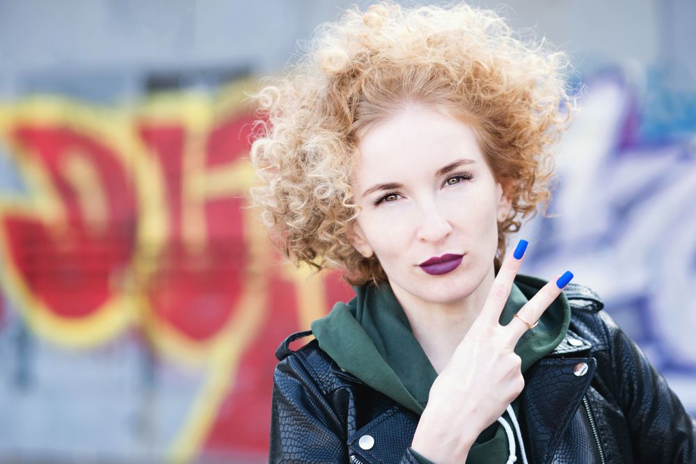 Curly haired female in leather jacket making peace sign outdoors
