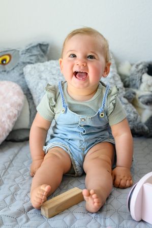 Cheerful baby sitting on bed looking at camera