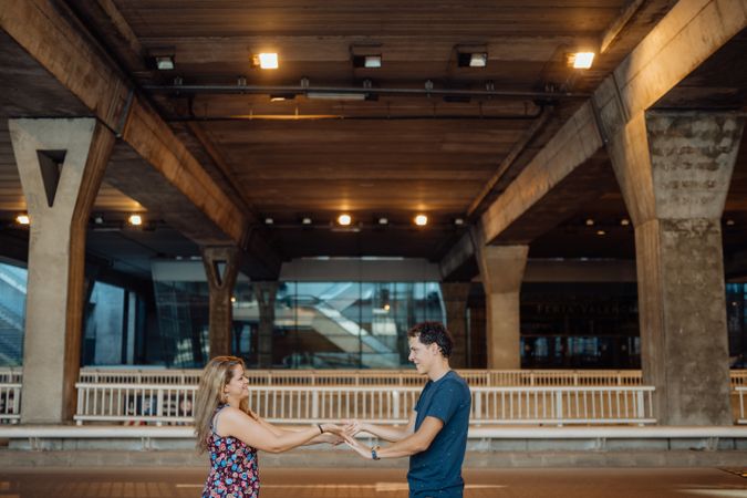 Woman and man clasping hands under large urban bridge