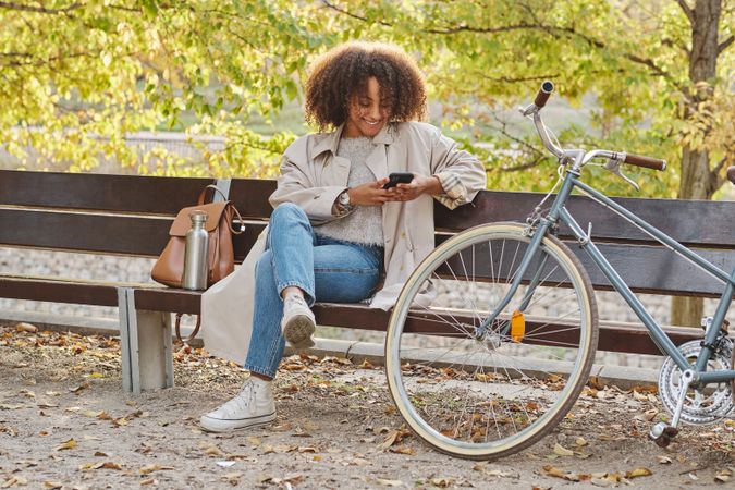 Smiling Black Latina woman sitting on bench with smartphone