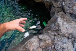 Crop man pulling plastic bag out of water