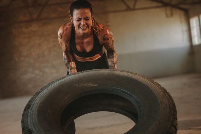 Fit female athlete working out with a huge tire, turning and flipping in cross workout space