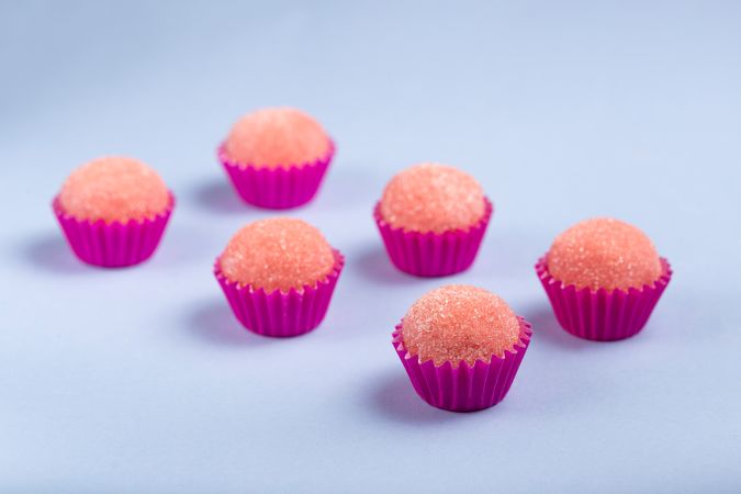 Pink strawberry truffles with sugar arranged on blue table