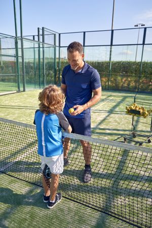 Coach with boy chatting during padel game on sports ground