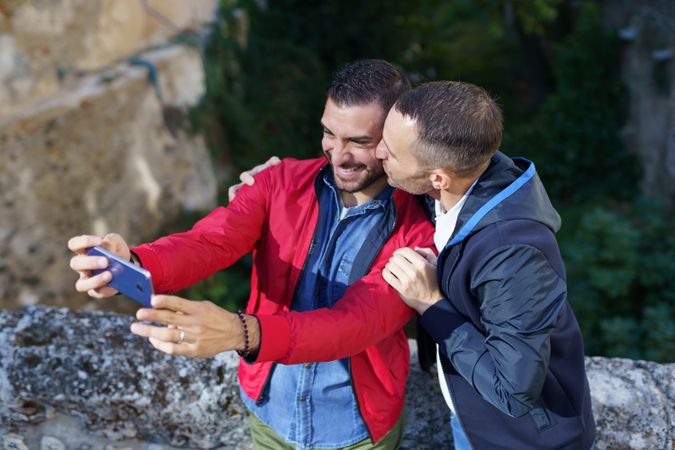 Two happy men taking selfie outside with a kiss on the cheek