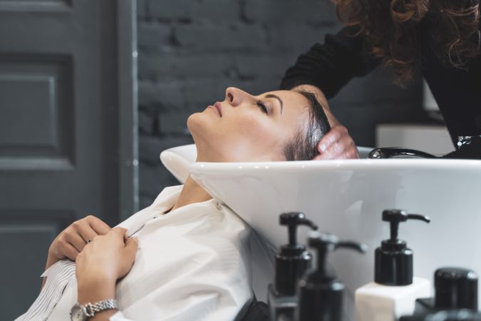 Stylist washing hair to young woman