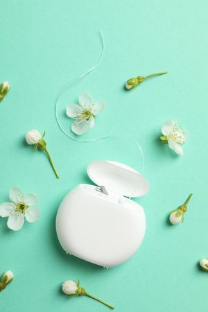 Dental floss and flowers on mint background, top view