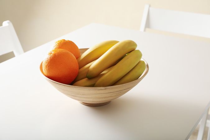 Bowl with oranges and bananas on table