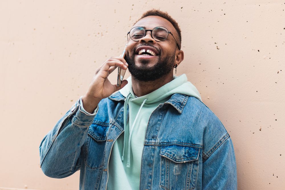 Cheerful Black man talking on phone near wall