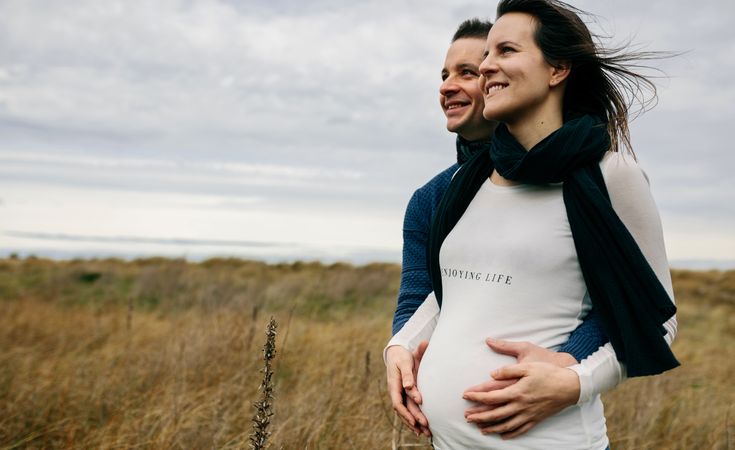 Pregnant woman with partner hugging and holding belly