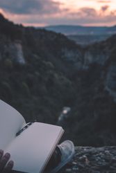 View to small river in canyon and legs of person with book sitting on the edge