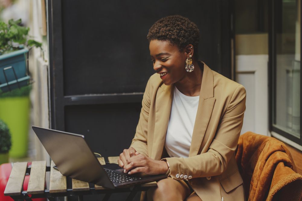 Smiling Black woman sitting at table with laptop in cafe