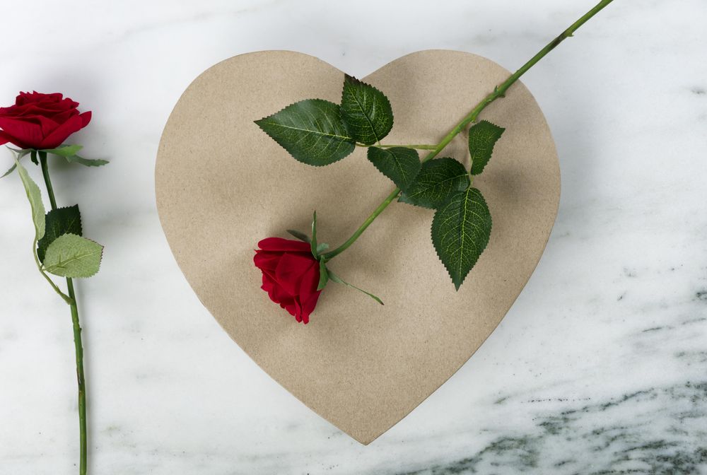 Happy Valentine’s Day with a large heart shape giftbox and red roses on marble stone