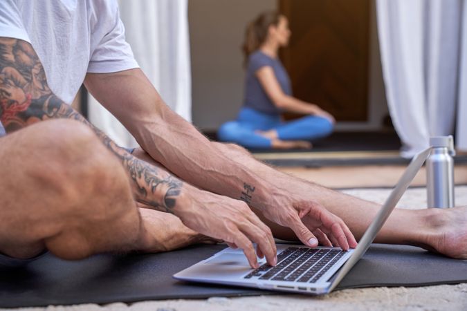 Crop man browsing laptop while woman doing yoga in yard